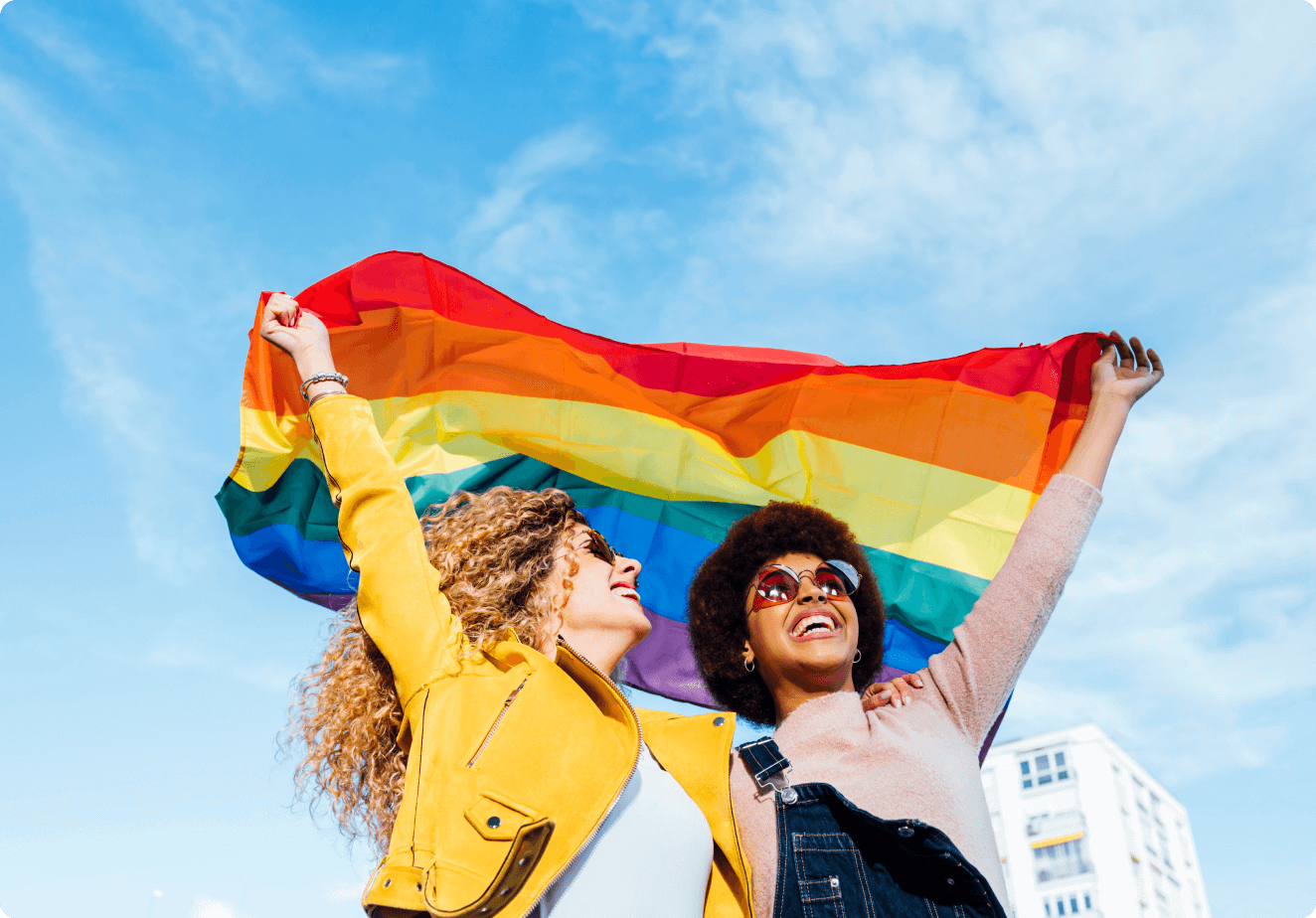 Imagem de duas pessoas sorridentes levantando a bandeira L G B T Q I A P N mais